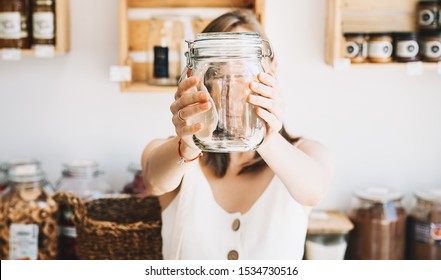 Woman in white linen dress with empty glass jar buying in sustainable plastic free grocery store. Girl with reusable cotton bag and wicker basket in zero waste shop. Minimalist low waste lifestyle - Powered by Shutterstock