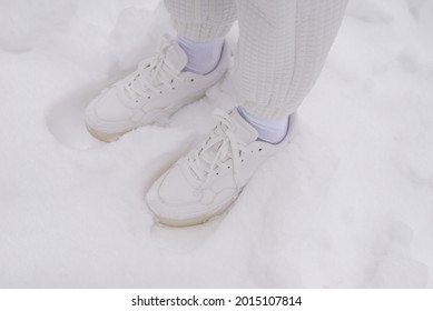 Woman In White Pants And White Sneakers Stands In A Snow. 