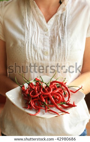 Woman in white shirt holding white ceramic plate laden with fresh red chili peppers