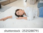 A woman in a white shirt in a mattress store. She examines the mattress she wants to buy.