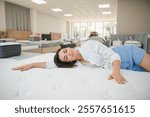 A woman in a white shirt in a mattress store. She examines the mattress she wants to buy.