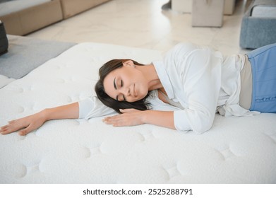 A woman in a white shirt in a mattress store. She examines the mattress she wants to buy.