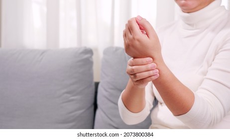 A woman in a white shirt sits on the sofa and massages her arms and wrists  To relax and to relieve pain  Health care concept - Shutterstock ID 2073800384