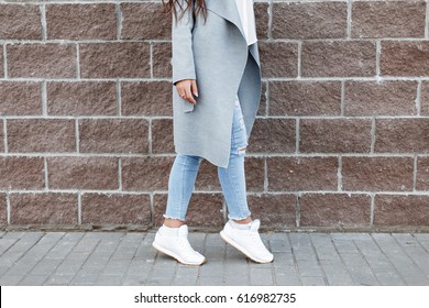 Woman In White Sneakers And Blue Jeans, Gray Coat Near A Brick Wall