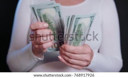 A woman in a white sweater holding cash (US Dollar banknotes) against a black background. Close-up shot