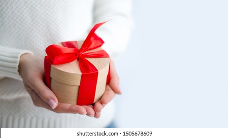 Woman in white sweater holding gift box with red ribbon in hands on white background - Shutterstock ID 1505678609