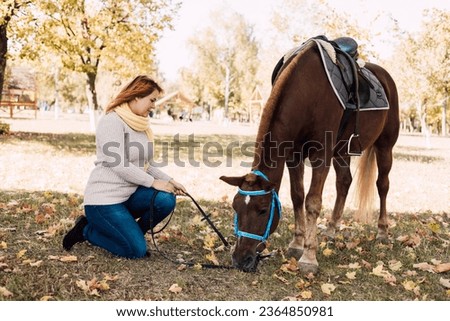A woman in a white sweater sits next to a brown horse. Autumn Walk. High quality photo