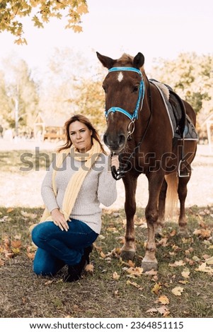 A woman in a white sweater sits next to a brown horse. Autumn Walk. High quality photo