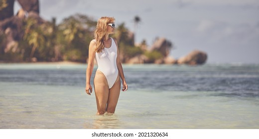 A woman in a white swimsuit stands in warm water on a tropical island
