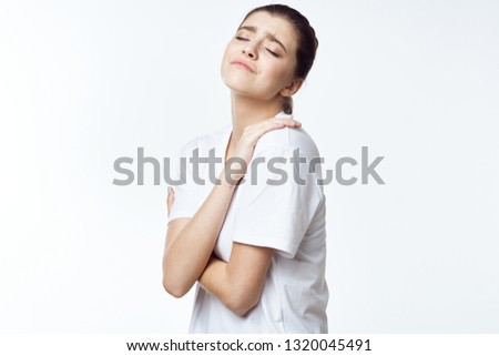 A woman in a white T-shirt touches herself with the pain in her shoulder