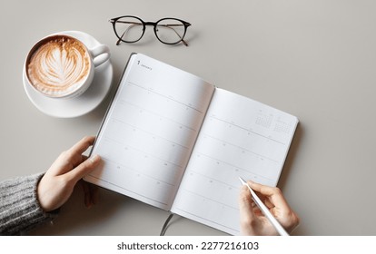 A woman who is keeping a diary note on a gray business table, background top view with glasses, coffee cups and copy space - Powered by Shutterstock