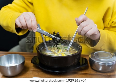 The woman who is putting seaweed flakes in bean sprout soup rice.