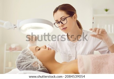 Woman who works as esthetician giving injection or hyaluronic acid filler to client under lamp magnifier. Youthful lady getting face treatment at beauty salon or clinic of aesthetic medicine ストックフォト © 