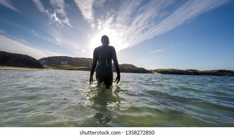 Woman Wild Swim In Wetsuit In Silhouette Walks Into Sea