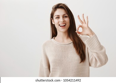Woman will make sure everything will go fine. Portrait of friendly assured caucasian girl smiling positively raising hand near face, showing okay or great gesture, being confident in good result - Shutterstock ID 1054211492