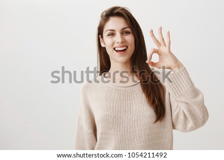 Woman will make sure everything will go fine. Portrait of friendly assured caucasian girl smiling positively raising hand near face, showing okay or great gesture, being confident in good result