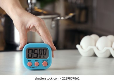 Woman winding up kitchen timer at white table indoors, closeup. Space for text - Powered by Shutterstock