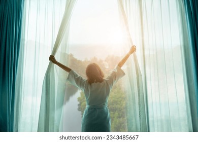 The woman was at the window in the bedroom. She opened the curtains on the window. In the morning and she looks at the view of mountains and trees at sunrise. - Powered by Shutterstock