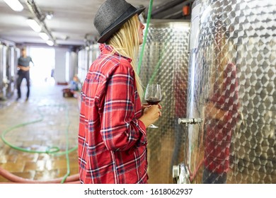 Woman As A Winemaker Trainee With Wine Glass In Front Of A Fermentation Tank In The Winery