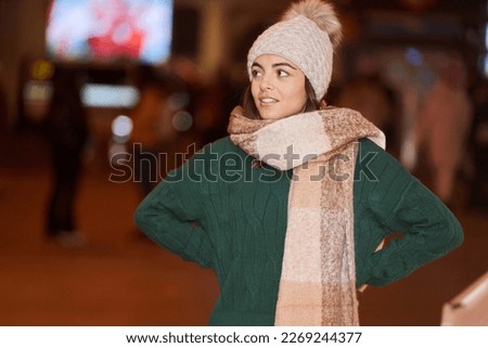 Woman in winter clothes and hat with arms at waist standing in the street. Winter and holidays concept.