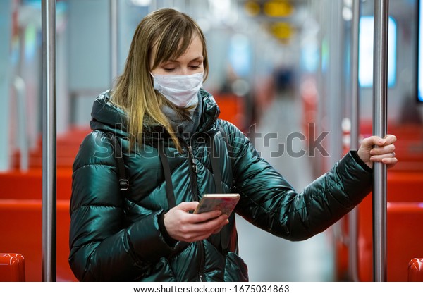 Woman in winter coat\
with protective mask on face standing in subway car, using phone,\
looking worried. Preventive measures in public places of epidemic\
regions. Finland, Espoo