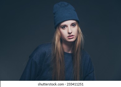 Woman Winter Fashion Wearing Blue Cap And Sweater. Long Blonde Hair. Studio Shot Against Grey.