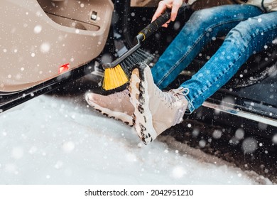Woman in winter in heavy snow brushes shoes from snow before getting into the car - car care
