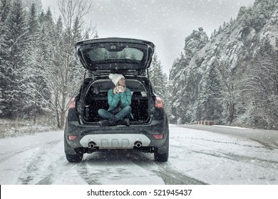 Woman at winter time. Yoyng female with hot tea in her hands sitting in black car at snowly winter day.