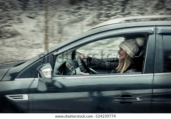 Woman at winter time. Yoyng female\
sitting and driving in black car at snowly winter\
day.