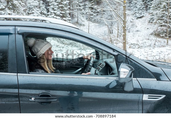 Woman at winter time. Yoyng female\
sitting and driving in black car at snowly winter\
day.