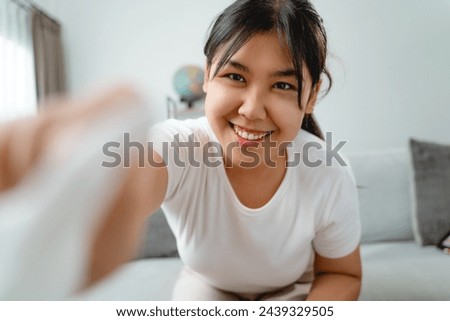 A woman is wiping cleaning the camera lens or screen monitor with paper towel She is wearing a white shirt and is sitting on a couch