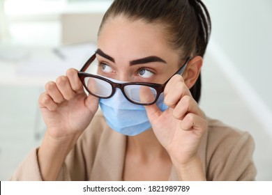 Woman Wiping Foggy Glasses Caused By Wearing Medical Mask Indoors, Closeup