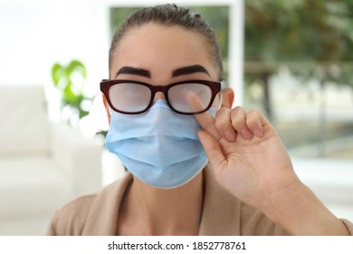 Woman Wiping Foggy Glasses Caused By Wearing Medical Mask Indoors, Closeup