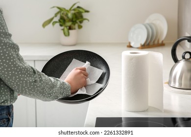 Woman wiping frying pan with paper towel in kitchen, closeup