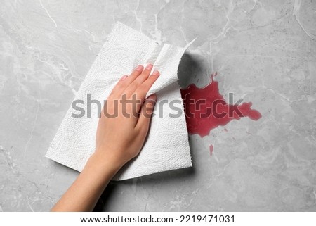 Woman wiping spilled juice with paper napkin on grey surface, top view