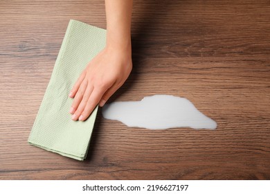 Woman Wiping Spilled Milk With Paper Napkin On Wooden Surface, Top View