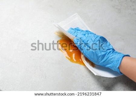 Woman wiping spilled sauce with paper towel on grey surface, closeup. Space for text