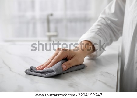 Woman wiping white marble table indoors, closeup