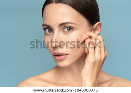 Woman without makeup touching cheeks after glycolic acid peel, has signs of aging skin on her face, looking at camera, isolated on studio blue background. Beauty skincare, cosmetology facial treatment
