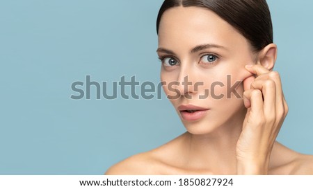 Woman without makeup touching cheeks after glycolic acid peel, has signs of aging skin on her face, looking at camera, isolated on studio blue background. Beauty skincare, cosmetology facial treatment