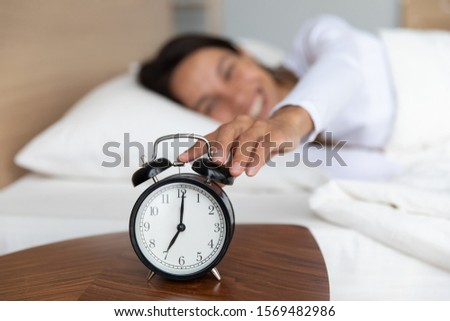Woman woke up at seven o'clock, close up focus to female extend hand turns off wind-up alarm clock on bedside table. Concept of enough healthy sleep, good morning, beginning of happy new wonderful day Foto stock © 