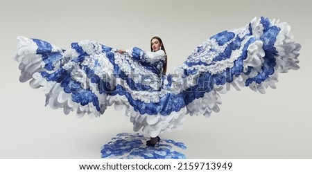 Woman in wonderful flying dress with blue and white waves. Drawing and ruffles on clothes. Model standing on the blue waves drawing                                