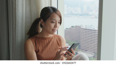 Woman work on cellphone and sit beside window