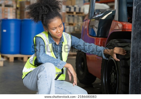 woman at work in storage\
warehouse wearing hard hat and hi visible vest not in good mood due\
to folklift flat tire puncher no able to distribute goods\
boxes\
