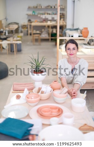 Woman in work wear in her workshop by table with handmade items