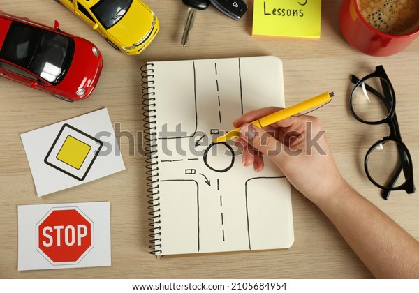 Woman with workbook for\
driving lessons and road signs at wooden table, top view. Passing\
license exam