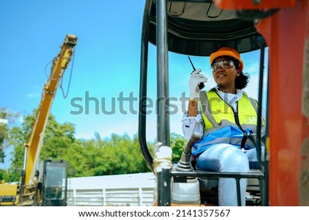 A woman worker driving a backhoe to dig a hole in a construction site holding a walkie talkie.African American female engineer wearing a hard hat and vest.
cute female with black skin gender equality.
