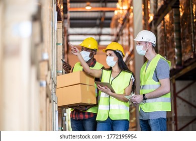 Woman worker hold tablet talking to man in warehouse store. Male and female engineers people wear safety hard helmet, vest and face mask checking storage box parcel in factory during covid 19 pandemic