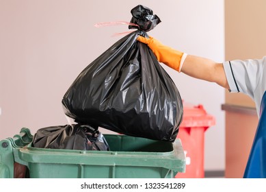 A Woman Worker Holding Black Garbage Bag Into Recycle Bin.Maid And Waste Bin At The Indoor Public Building.Green Bin With Waste Bag On Floor In The Hospital.Infectious Control. 