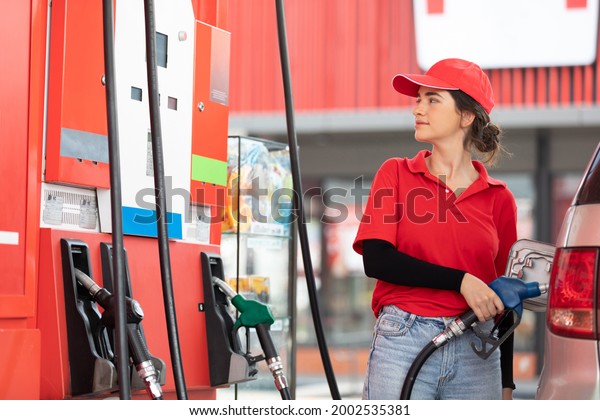 woman worker holding petrol hose and refueling\
vehicle or car at gas\
station